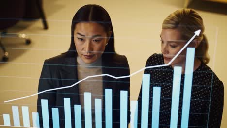 two women examine financial graphs and charts in a contemporary office environment. they discuss important metrics and trends while collaborating on a project.