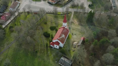 aerial view of a white church with red roof on a sunny spring day, wide angle drone shot moving forward, tilt down