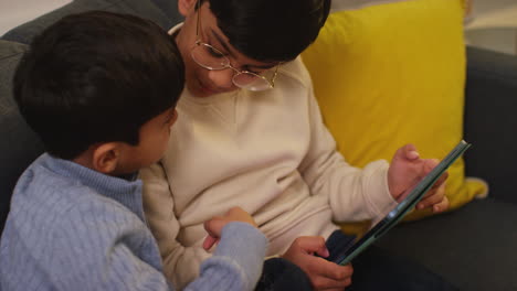 two young boys sitting on sofa at home playing games or streaming onto digital tablet 11