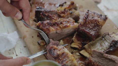 group of friends eating and cutting pieces of beef ribs asado on cutting board