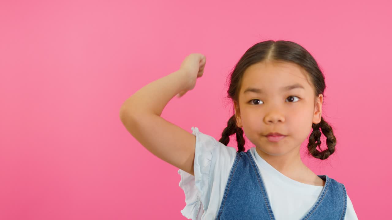 Young girl with pigtails gives enthusiastic thumbs up, cheerful expression, bright pink background, studio lighting