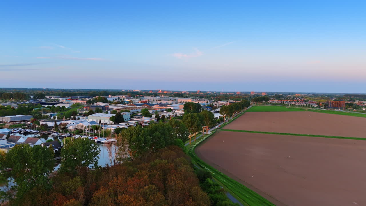 Bridge over the canal leading to the road to a town in the Netherlands. Cozy residential area at sunset. Aerial perspective.