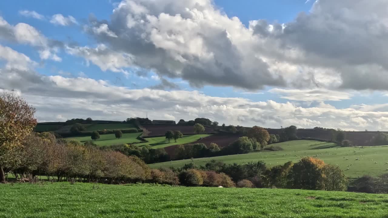 Aerial footage capturing the tranquil beauty of the South Downs in England with rolling green hills, lush pastures, and dramatic clouds under clear skies. Ideal for nature and landscape enthusiasts