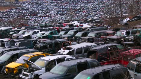 cars sit in rows in a vast junkyard in the snow