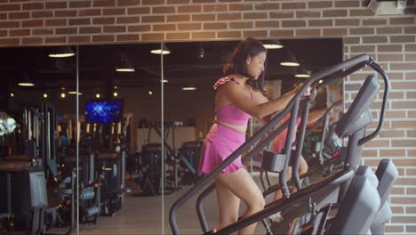 una mujer joven usando una máquina de pasos en el gimnasio con ropa deportiva