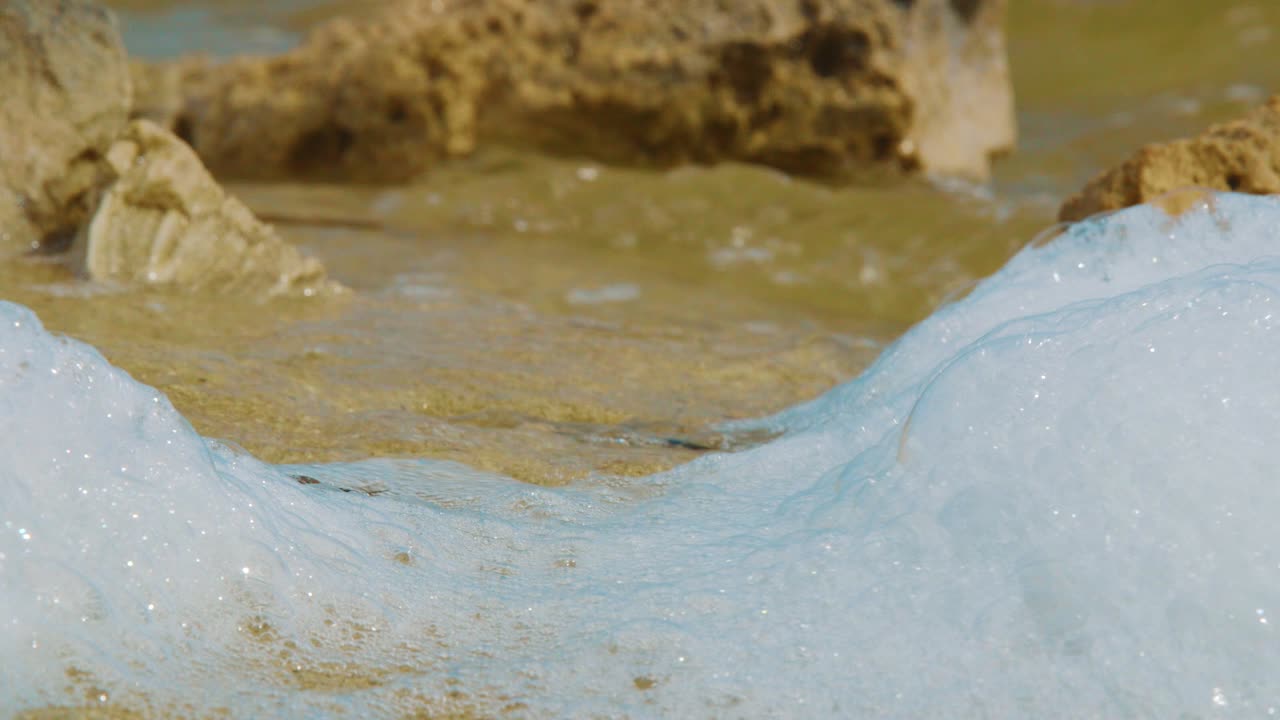 Saltvandsskum skyllet i land på en tropisk strand i Kralendijk, Bonaire - nærbillede.