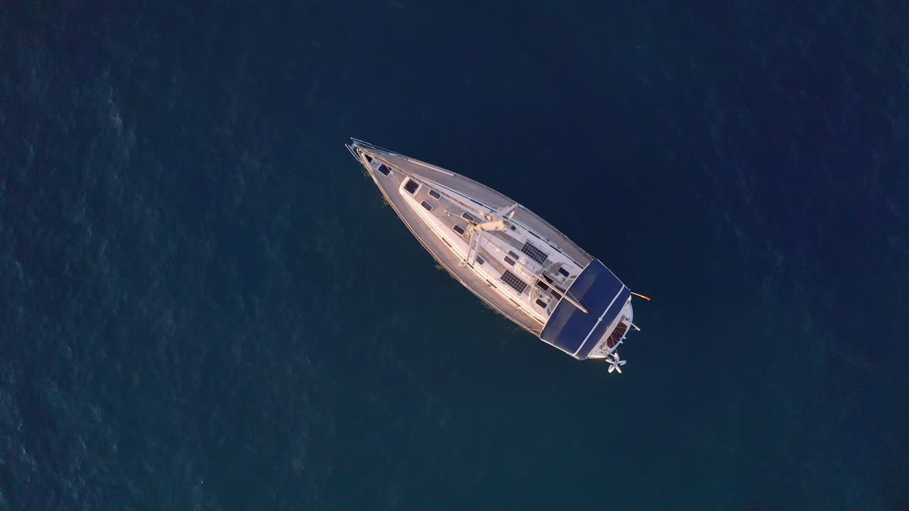 Ripresa 4K dall'alto di un lussuoso yacht privato con un albero maestro alto su un mare blu scuro che getta l'ancora vicino a una costa rocciosa in una soleggiata giornata estiva.