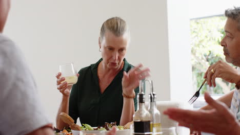 enjoying lunch, senior friends conversing and sharing meal at dining table
