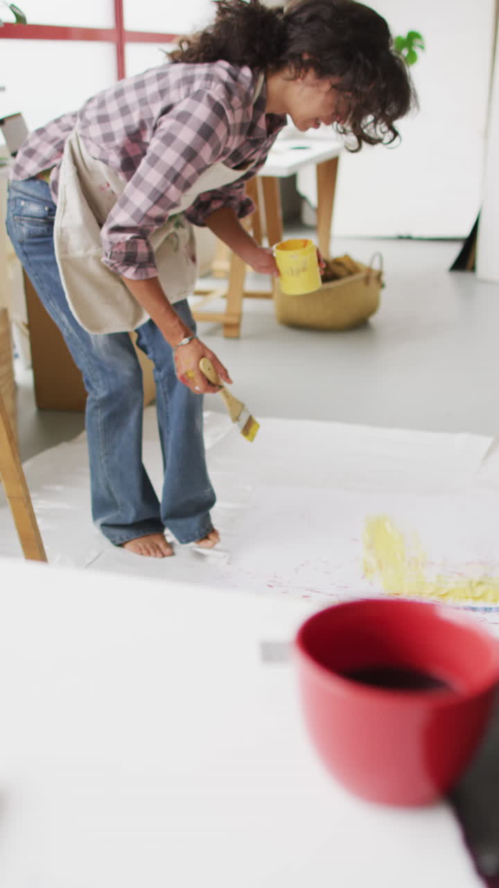 video vertical de una artista femenina biracial pintando en el suelo en el estudio