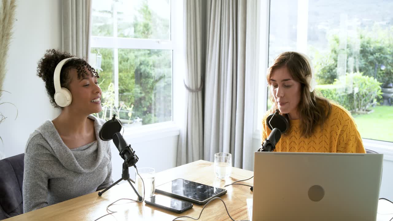 Çeşitli kadın ortak sunucular, pencere kenarındaki masada podcast kaydediyor, mikrofonları ayarlayıp beşlik çakıyor.