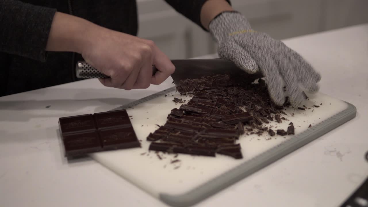 una niña corta chocolate negro antes de derretirlo para hacer galletas de mantequilla millonarias mientras usa guantes de seguridad-4