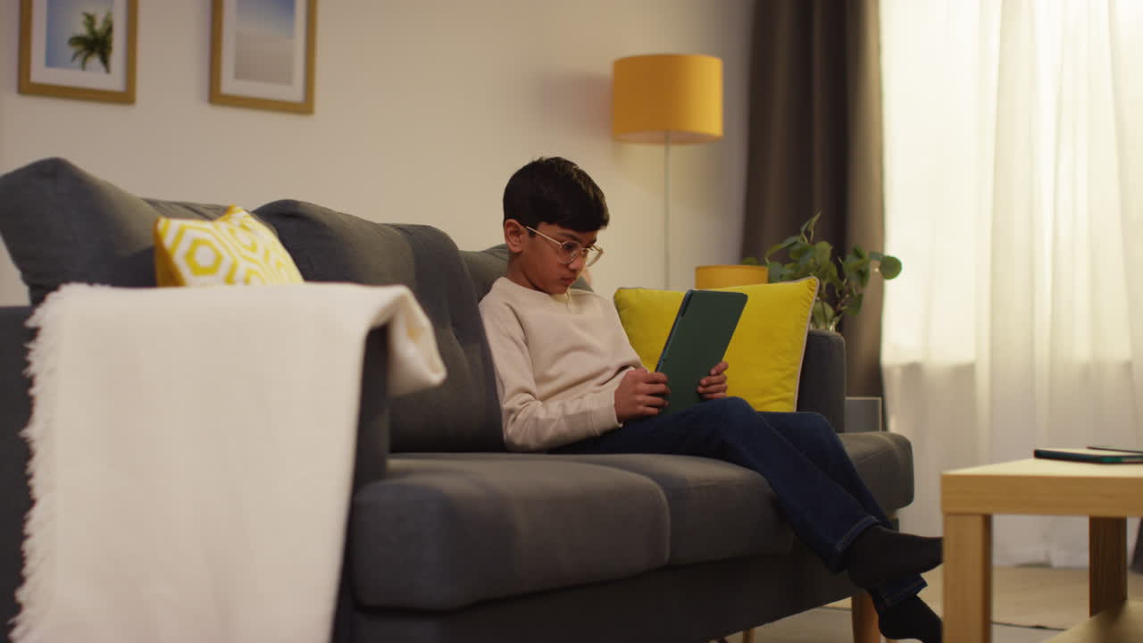 Young Boy Sitting On Sofa At Home Playing Games Or Streaming Onto Digital Tablet 7
