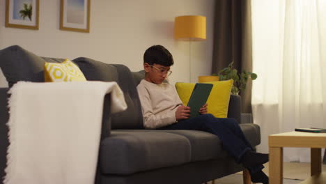 young boy sitting on sofa at home playing games or streaming onto digital tablet 7