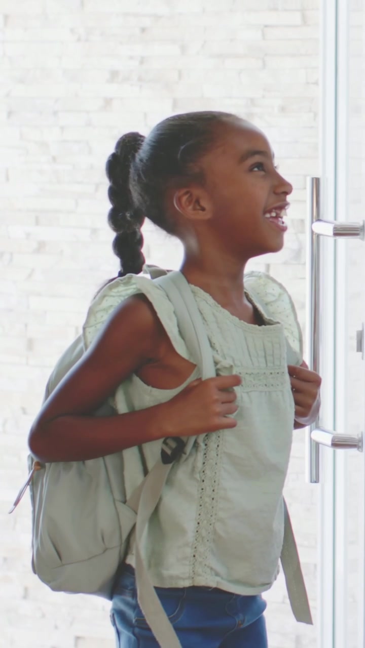 Vertical video: Door opening youth wearing green top and jeans entering foyer, adjusting backpack
