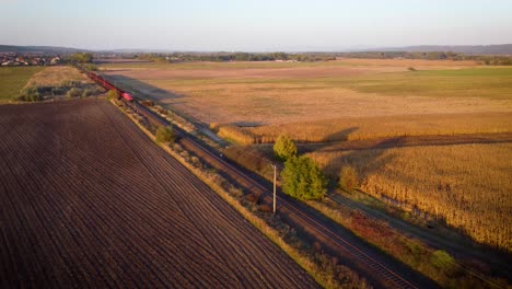 train passing by factory with cargo on farm fields in the sunset