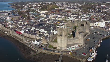 an aerial view of caernarfon castle on a sunny day, flying left to right around the castle while zooming in, gwynedd, north wales, uk