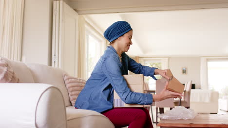 happy biracial woman in hijab unpacking boxes at home, copy space, slow motion