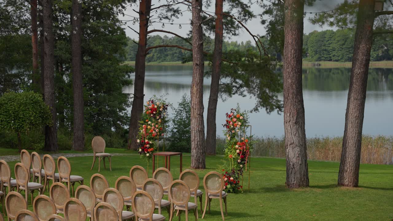 Un allestimento elegante per un matrimonio all'aperto, con sedie e archi floreali in riva a un lago tranquillo. L'ambiente naturale offre uno sfondo sereno e pittoresco per eventi speciali