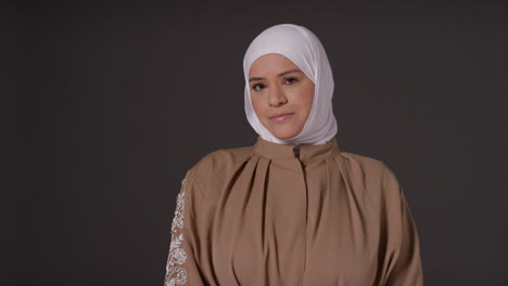 studio portrait of muslim woman wearing hijab against plain dark background