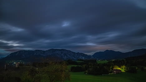 timelapse of impressive mountain landscape in austria with fast moving clouds and view of the imposing mountains and a house, which is illuminated and sets warm light accents in the evening