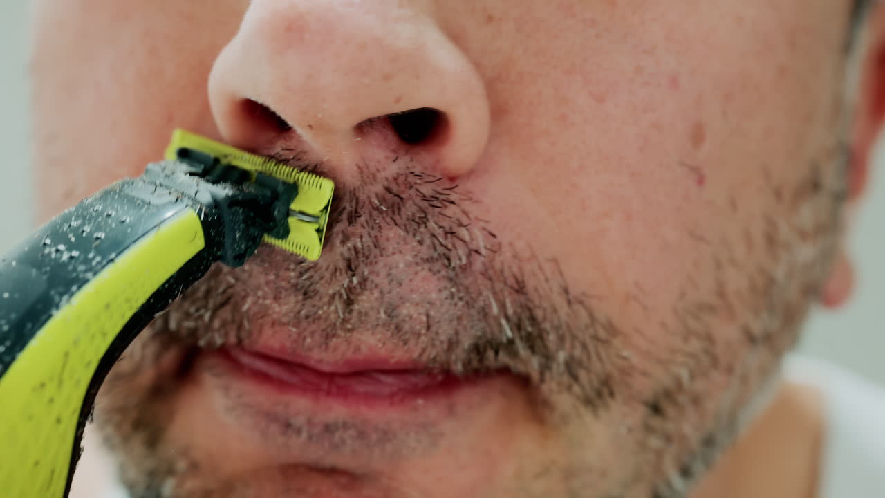 Close up of a man using an electric razor to trim facial hair in the bathroom