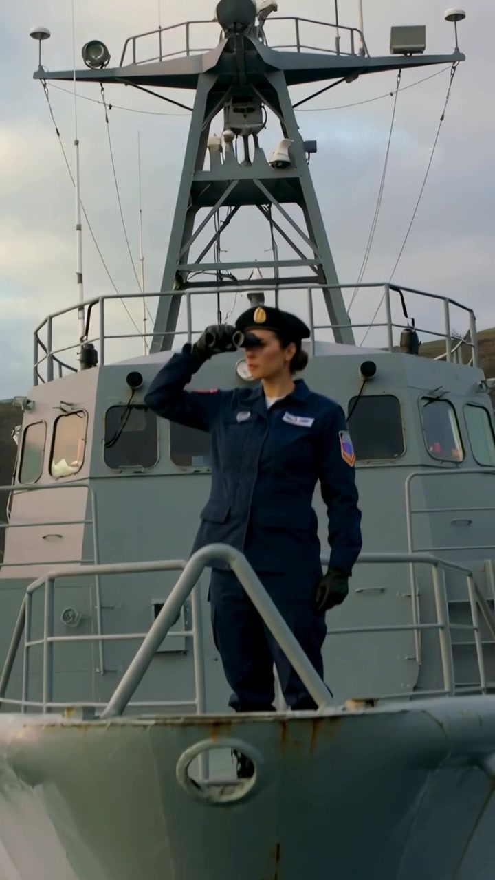 Video verticale: Prua che taglia la scia, imbarcazione che mostra una donna in uniforme che saluta, poi che scruta per la guardia.