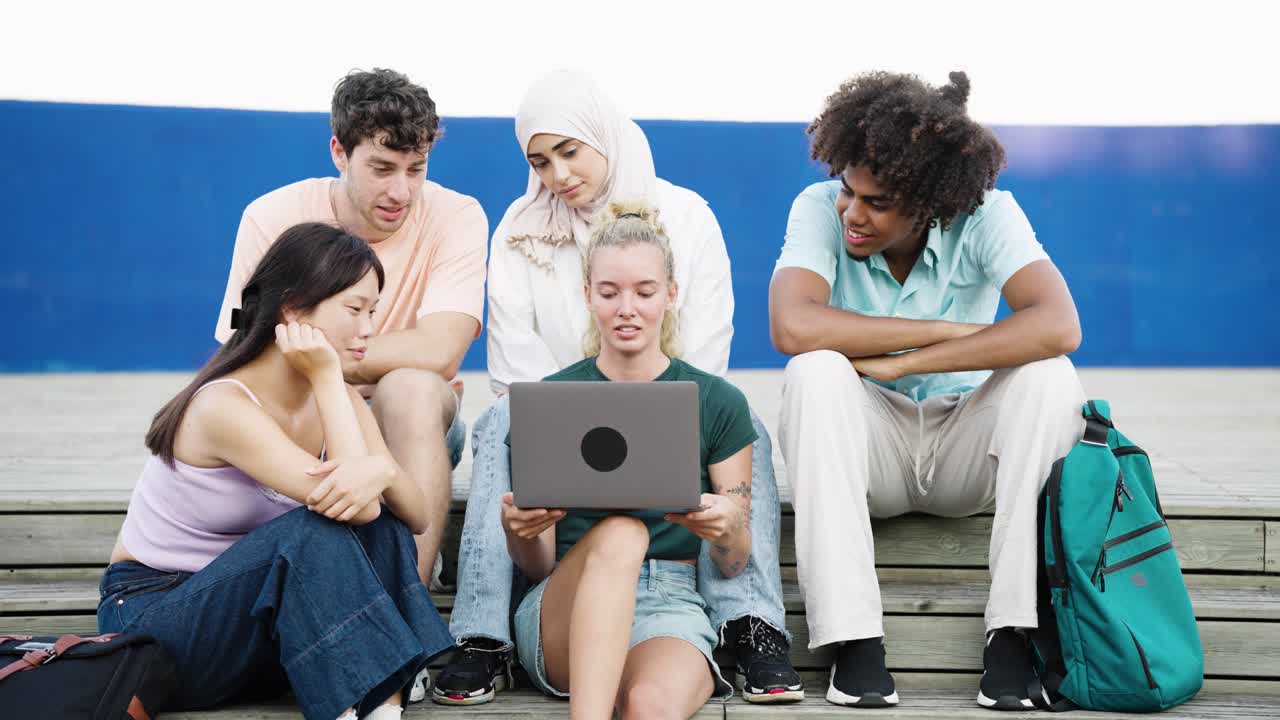 Gruppo eterogeneo di giovani adulti che condividono un laptop all'aperto