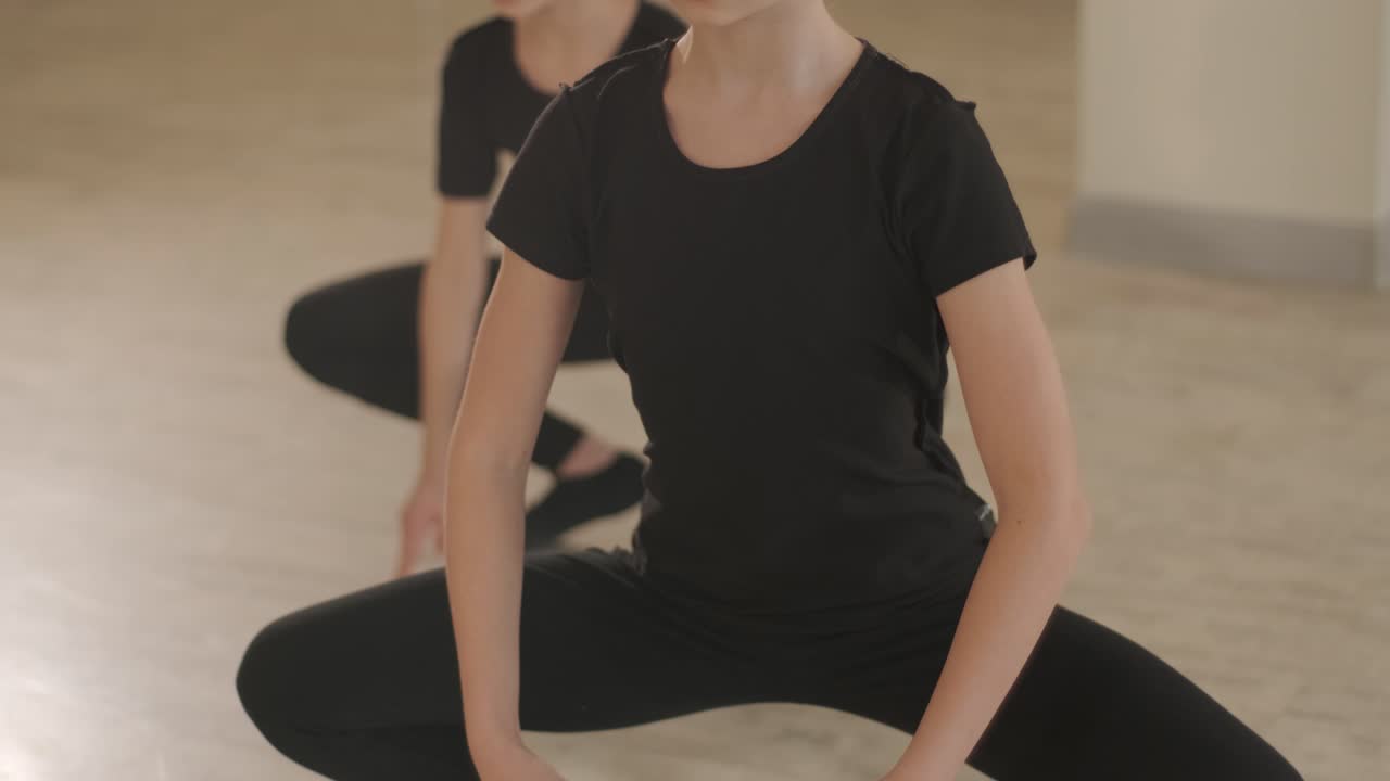 un grupo de jóvenes estudiantes de ballet con ropa de baile negra practicando posiciones en un amplio estudio de ballet con pisos de madera y barras montadas en la pared. expresiones enfocadas y movimientos sincronizados.