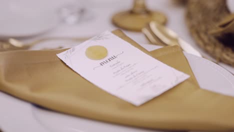 close up of a wedding menu card placed on a folded golden napkin atop a white plate