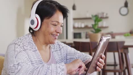 african american senior woman wearing headphones using digital tablet sitting on the couch at home