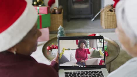 dos amigas mayores diversas que usan una computadora portátil para una videollamada de navidad con una mujer en la pantalla