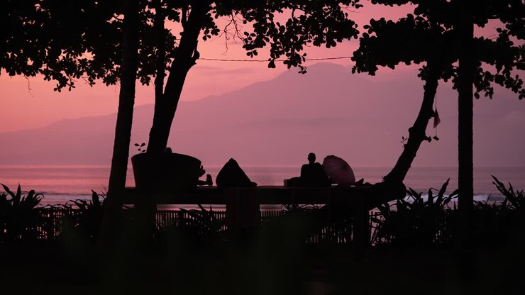 Silhouetted man sitting on a deck on an island beach watching a beautiful pink sunset