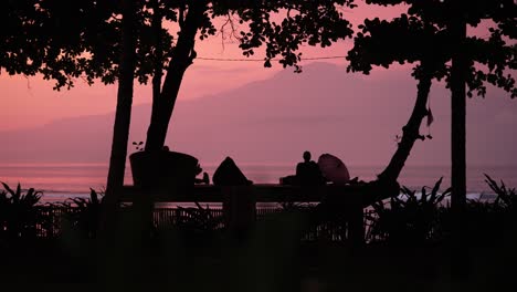 Silhouette-Eines-Mannes,-Der-Auf-Einem-Deck-An-Einem-Inselstrand-Sitzt-Und-Einen-Wunderschönen-Rosa-Sonnenuntergang-Beobachtet