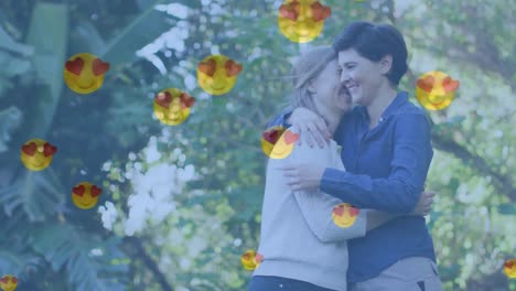 animación de emojis de corazón sobre una feliz pareja de mujeres caucásicas enamoradas abrazándose