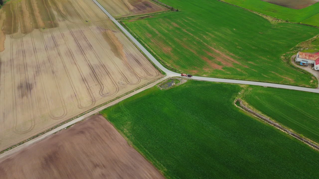 Aerial shot of a farmer driving his tractor in rural countryside roads in Norway
