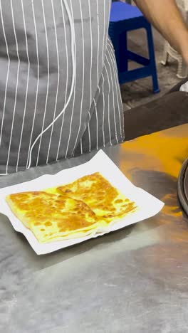 un vendedor callejero en phuket prepara y sirve roti de plátano, mostrando técnicas tradicionales de comida callejera tailandesa en un entorno vibrante