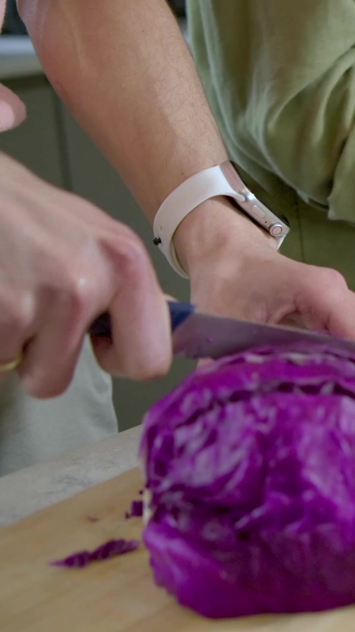 Vertical video: Reaching for knife, cook holding and slicing cabbage on board in kitchen for salad