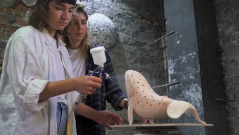dos mujeres pintando una escultura de ballena de cerámica