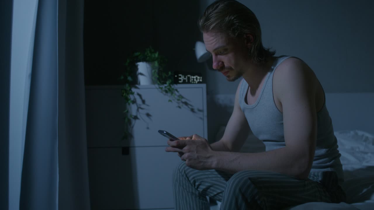 hombre estresado en la cama usando teléfono inteligente por la noche