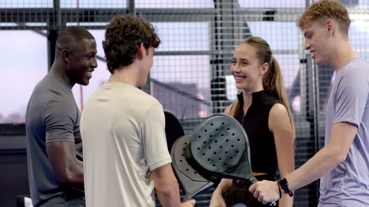 Group of young adults enjoying padel tennis on indoor court, holding rackets and smiling