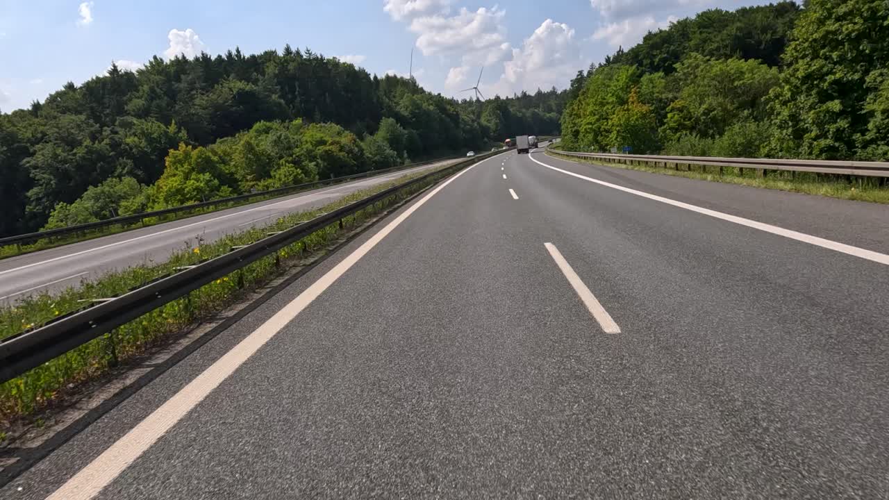 Vehicles travel on a sunlit highway through green countryside, wide angle, steady camera, summer daylight