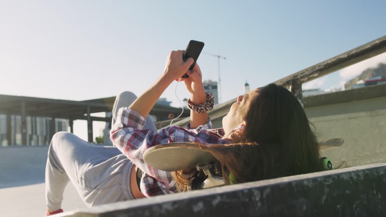 Caucasian woman, lying, using smartphone at a skatepark on sunny day