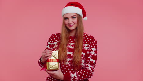 Cheerful-lovely-girl-in-sweater-Santa-hat-presenting-one-Christmas-box,-excited-by-holiday-gift