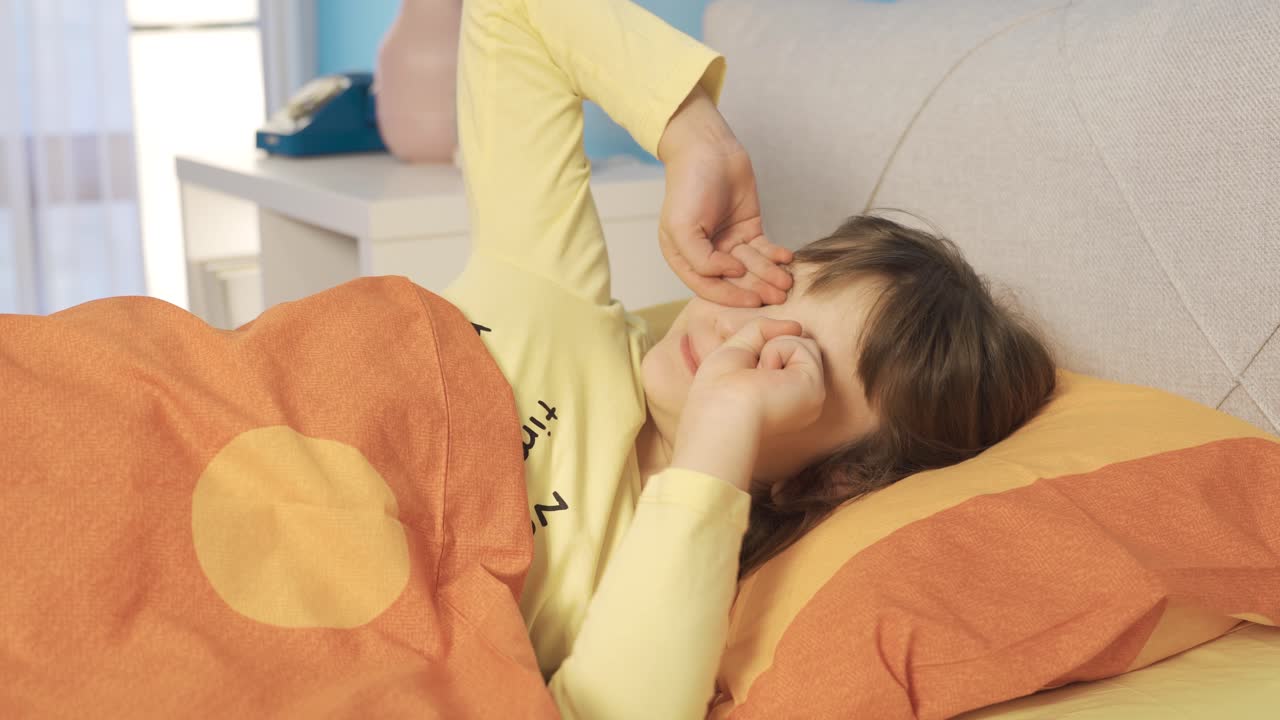 침대에 누워 있는 작은 소녀가 깨어납니다. 학교에 가고, 아침 식사를 위해 깨어납니다.