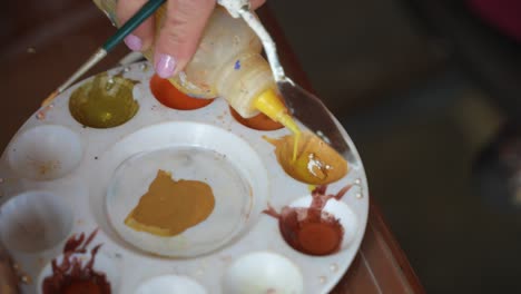 artist adding yellow paint to a palette from a bottle, close up