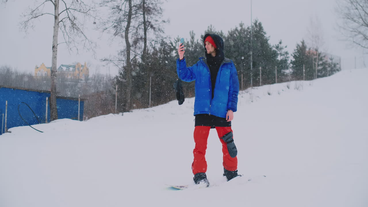 스키 슬로프에서 운전하는 동안 스마트폰을 사용하는 스노보더의 슬로우 모션 샷