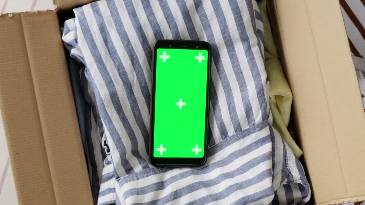 vista superior de la maqueta de pantalla verde del teléfono en una caja con ropa usada.