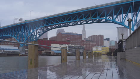 cleveland, ohio boardwalk passing under blue bridge with city in background on a rainy day