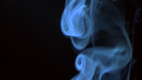 un goteo de humo azul lentamente ondulando girando hacia arriba. humo de cigarro soplando hacia arriba. primer plano, aislado sobre un fondo negro.