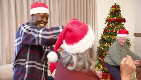 Happy-diverse-male-and-female-senior-friends-in-christmas-hats-dancing-at-home,-slow-motion